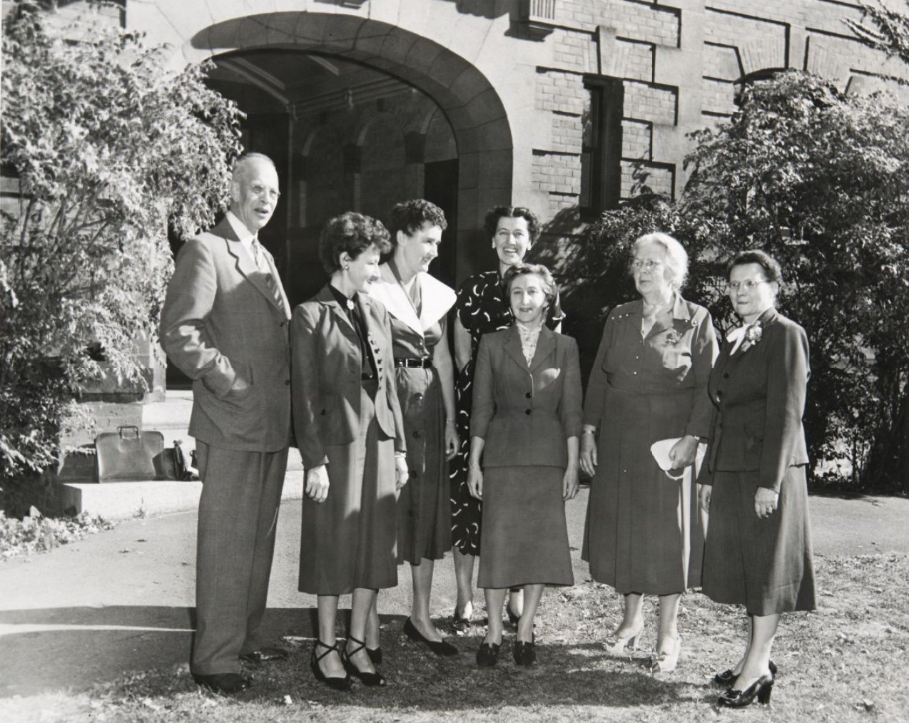 Grupo de mujeres y un hombre delante de un arco.