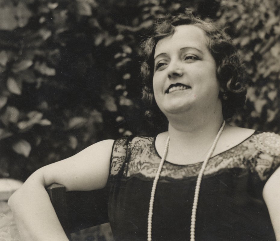 Retrato de mujer sonriente con un arbusto de fondo.