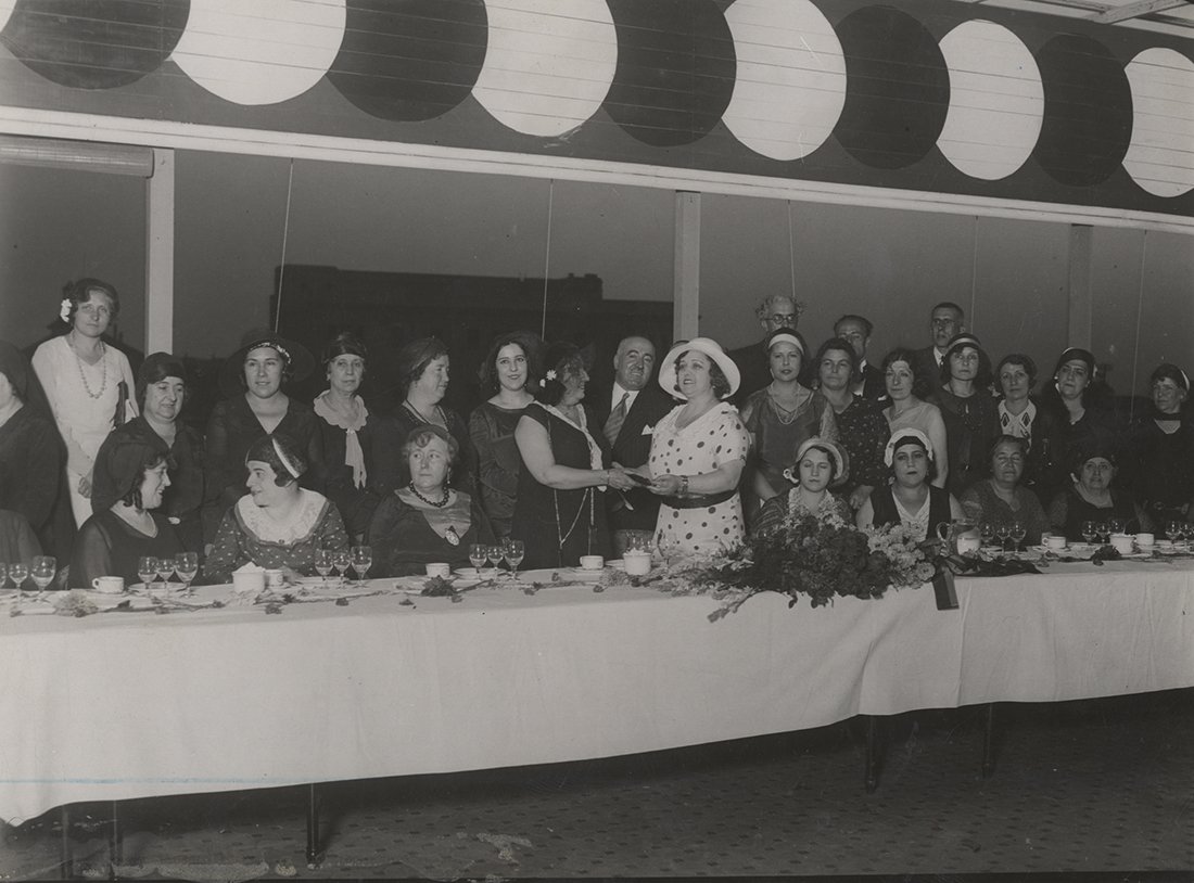 Mujer recibiendo un premio, rodeada de un grupo numeroso de mujeres, en una caseta.