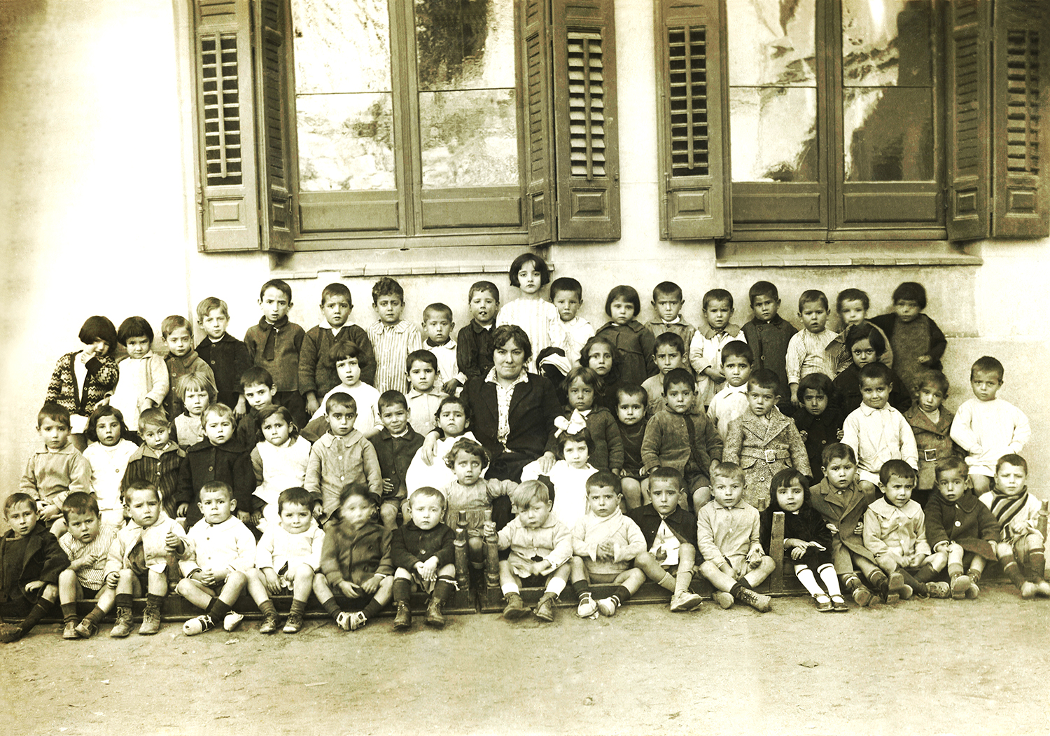Mujer rodeada de niños en el patio de un colegio.