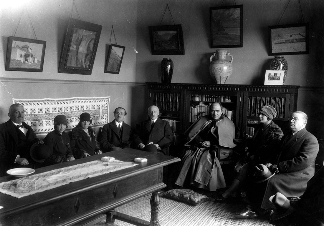Grupo de mujeres y hombres sentados en el interior de una casa.