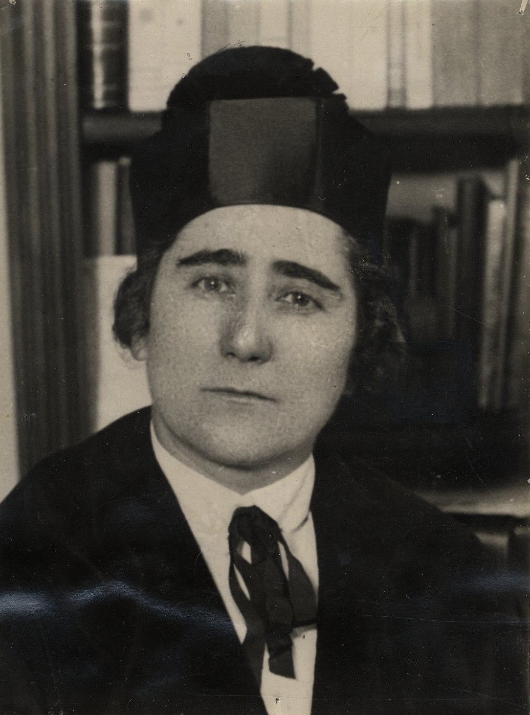 Retrato de mujer con traje de doctorado delante de una estantería.