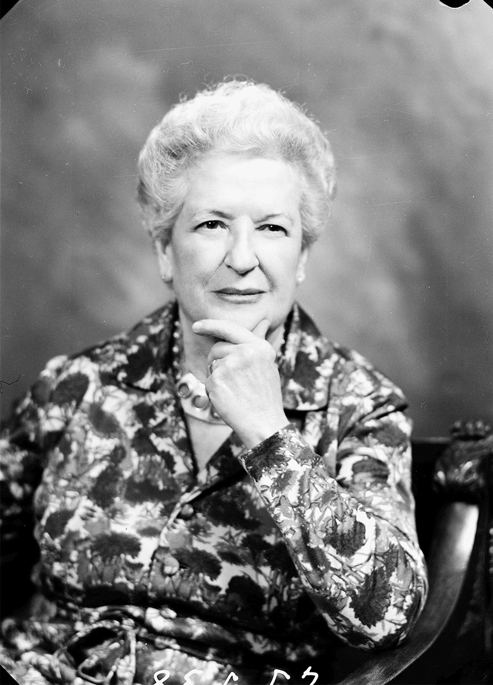 Retrato de mujer con una camisa de flores y la mano apoyada en la barbilla.