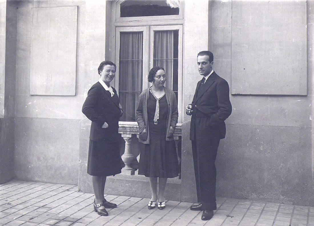 Dos mujeres y un hombre de pie delante de una ventana en la calle.