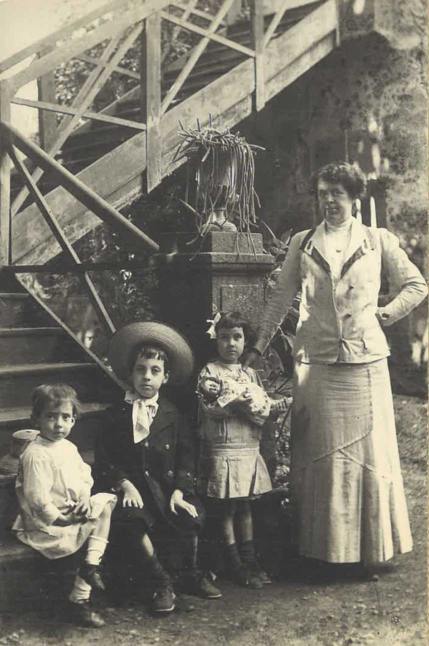 Mujer de pie junto a tres niños, al lado de una escalera en la calle.