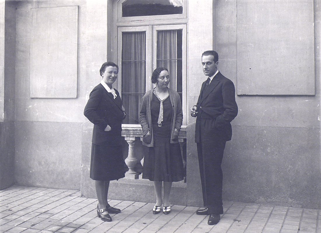 Dos mujeres y un hombre delante de una ventana.