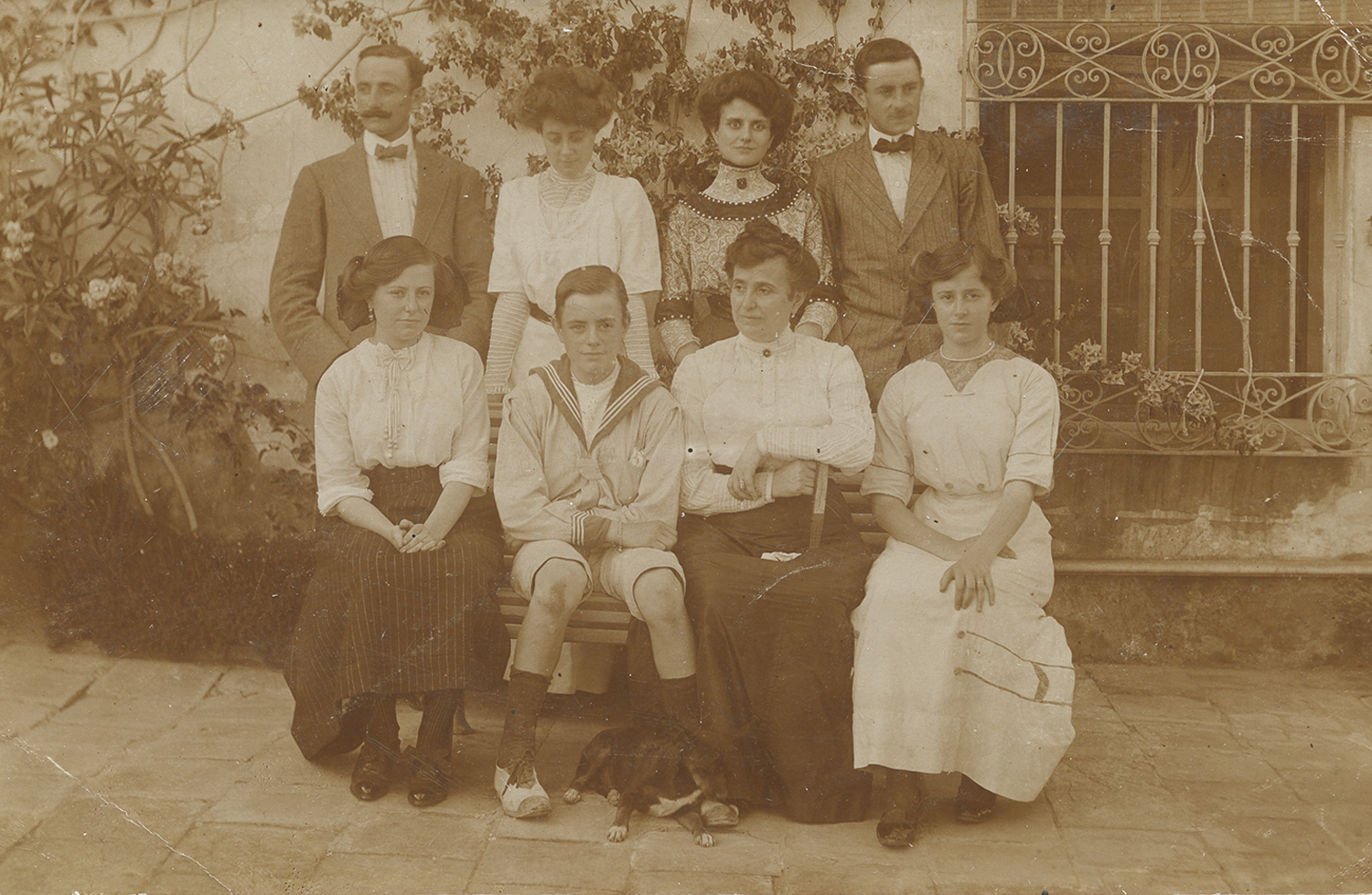 Retrato de familia en el exterior de una vivienda, con cuatro personas sentadas y cuatro de pie.