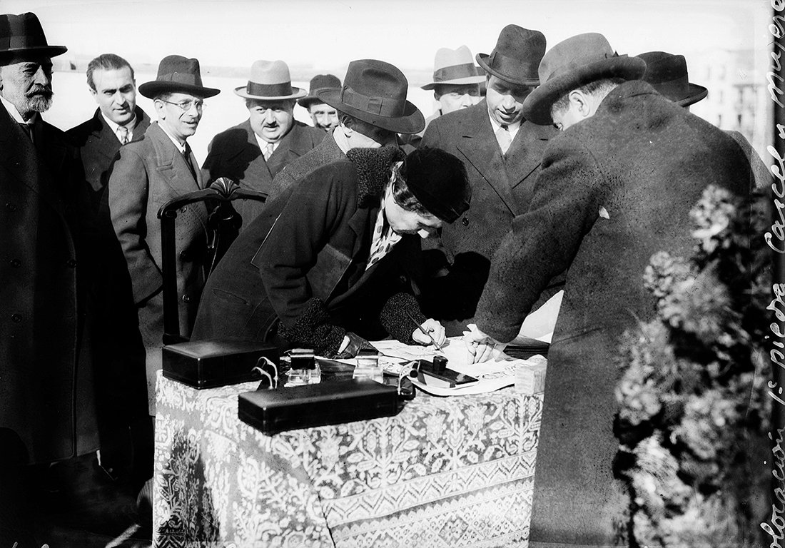 Mujer firmando con un grupo de hombres a su alrededor.