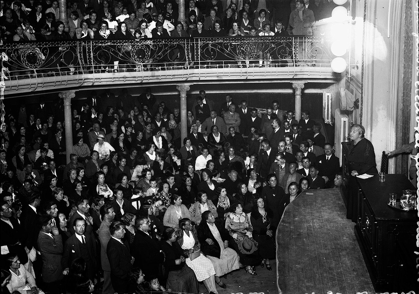 Mujer dando un discurso en un teatro frente a una multitud.