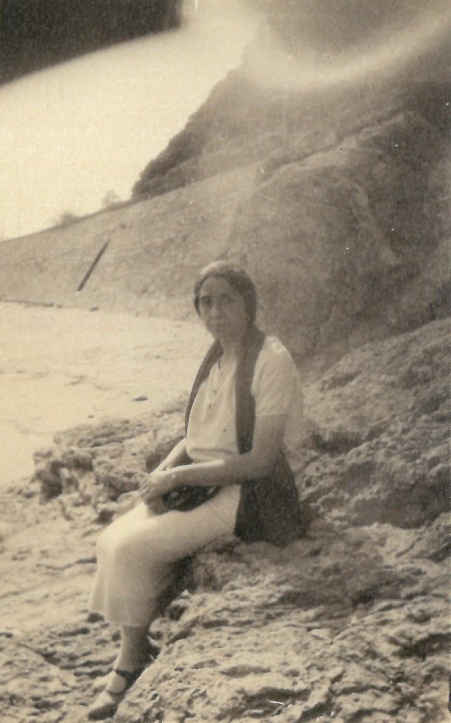 Mujer sentada en unas piedras en una playa.