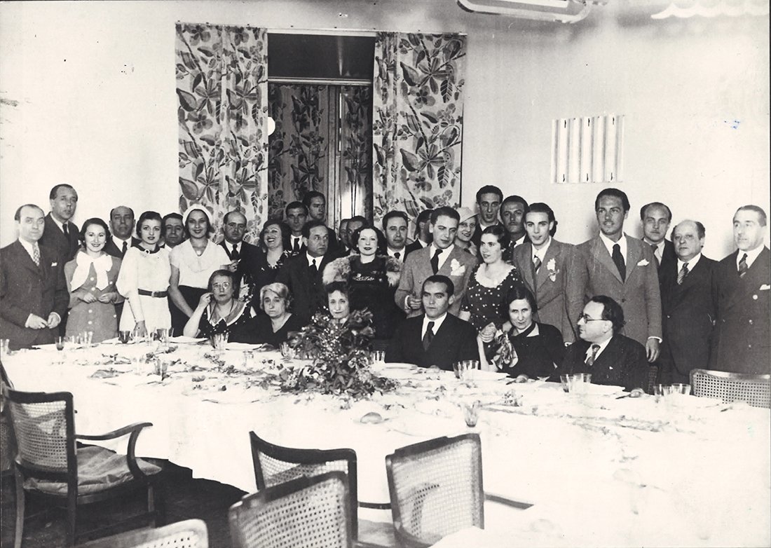 Grupo de hombres y mujeres alrededor de una gran mesa de comedor
