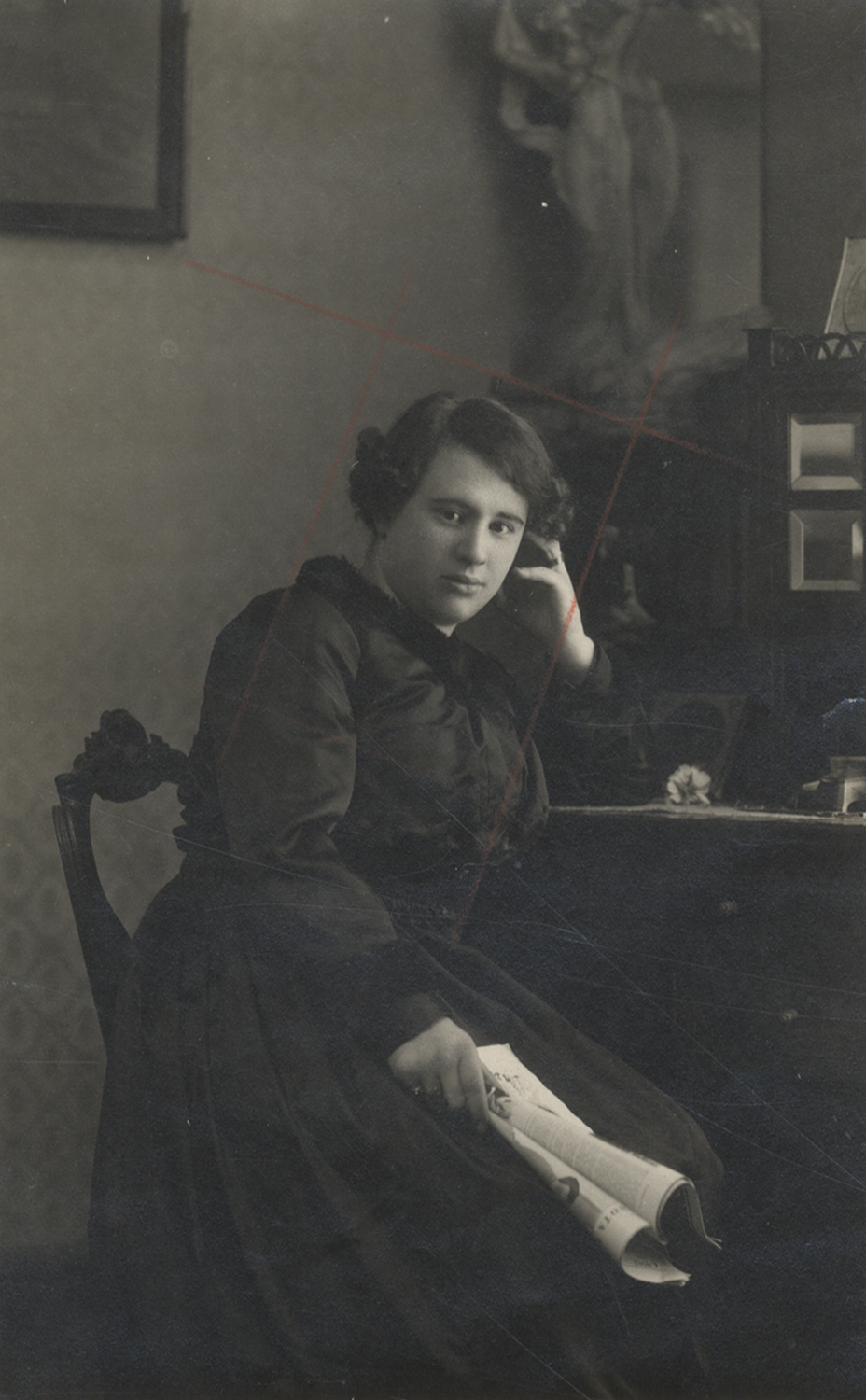 Mujer sentada con un periódico en la mano y la otra apoyada en la cabeza.