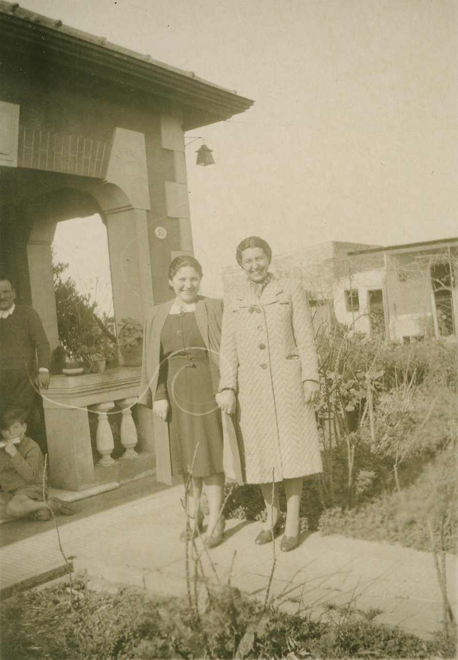 Dos mujeres posando sonrientes delante de una casa.