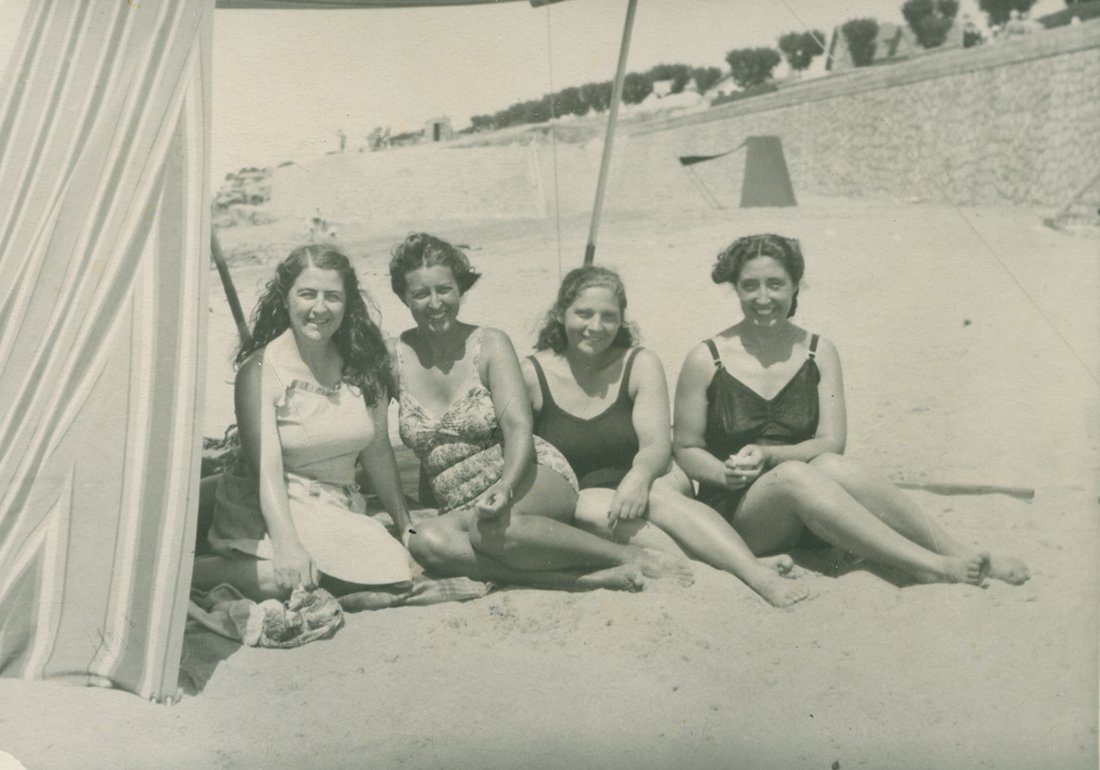 Cuatro mujeres en bañador sentadas en una playa.