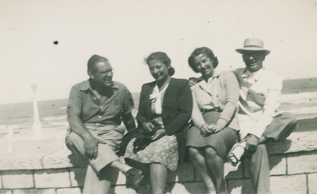 Dos hombres y dos mujeres sentados en el muro de una playa.