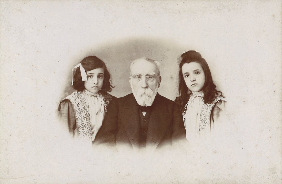 Retrato de dos niñas a los lados de su abuelo.