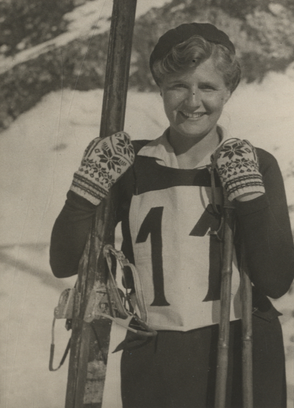 Mujer con guantes y unos esquíes en la mano.