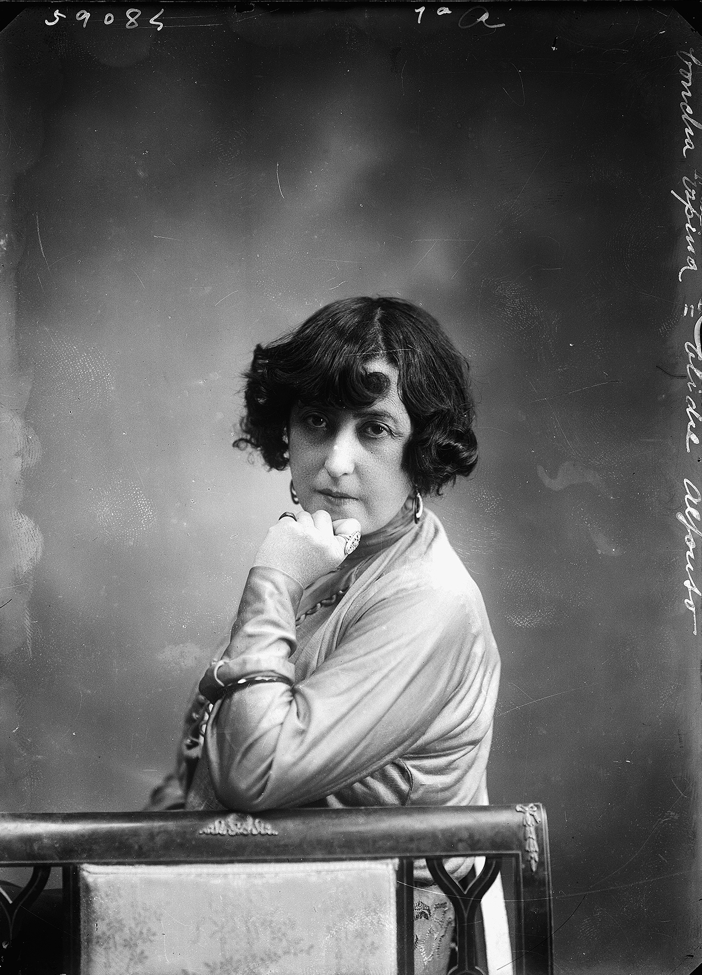 Retrato de mujer con el brazo apoyado en una silla y la barbilla en la mano.