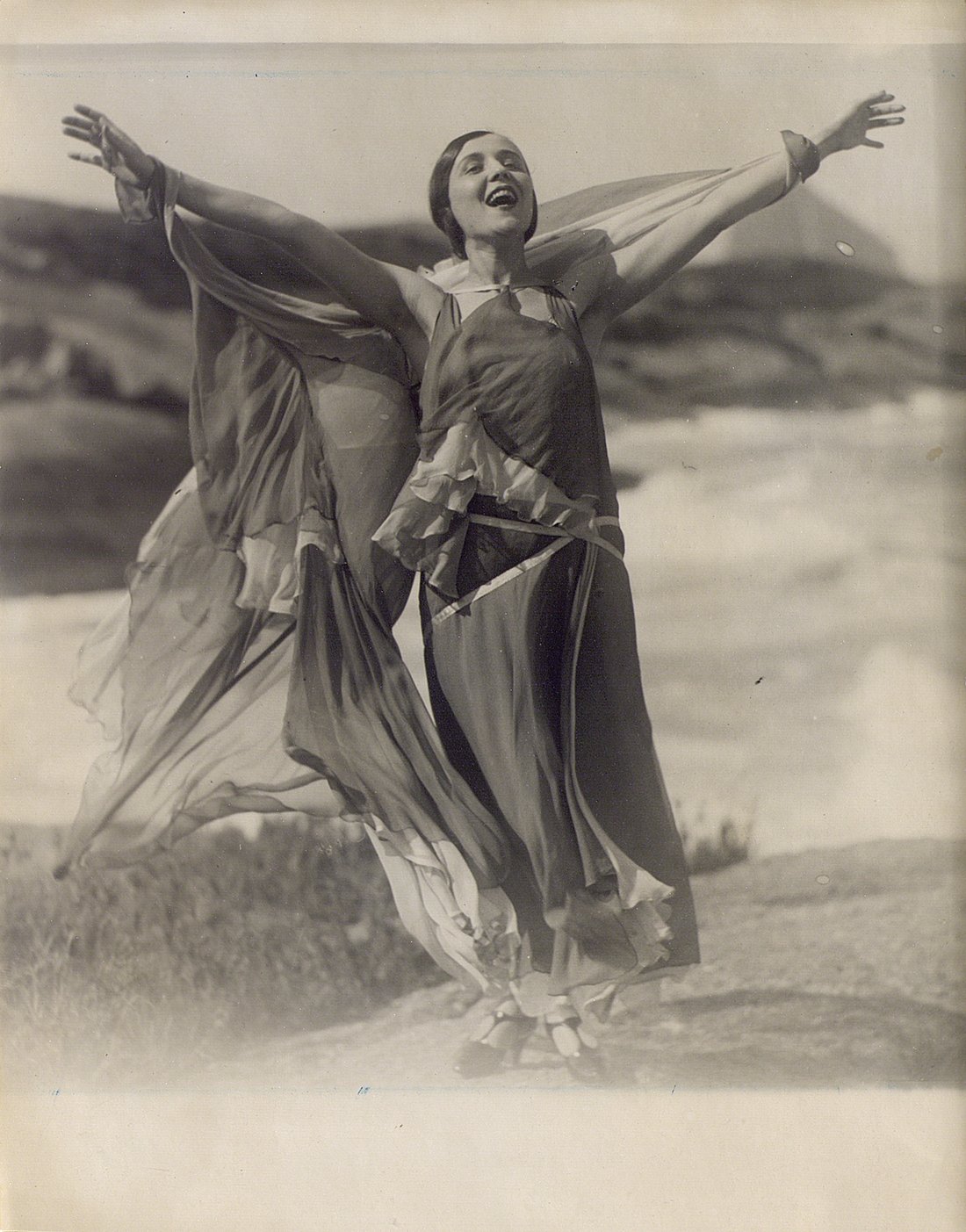 Mujer en la playa con los brazos abiertos cantando.