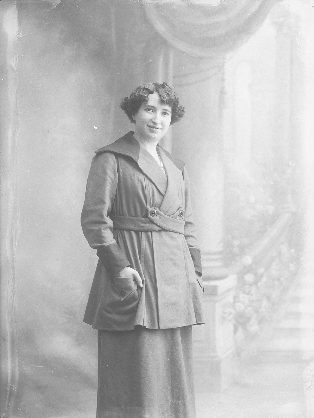 Mujer de pie con abrigo delante de unas escaleras.