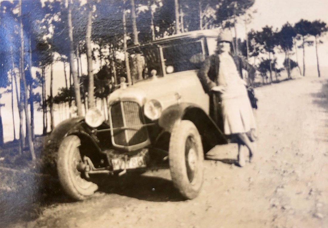 Mujer posando al lado de un coche en una carretera.