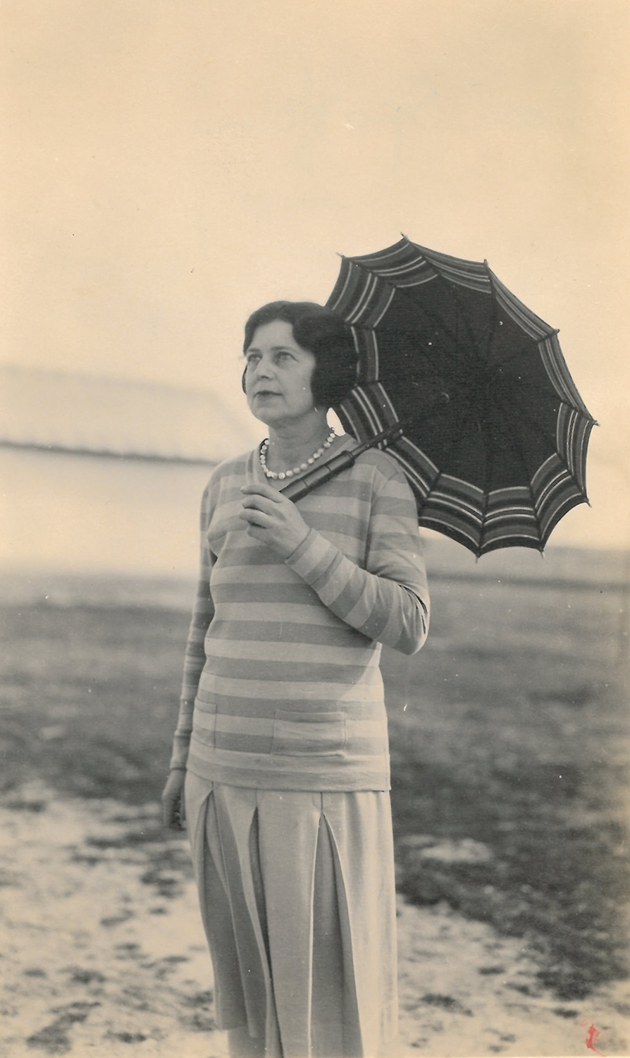 Mujer en la playa con sombrilla abierta en la mano.